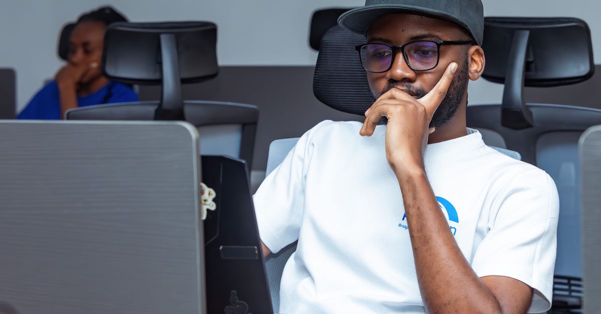 A focused African technology professional working at a computer in an open-plan office.