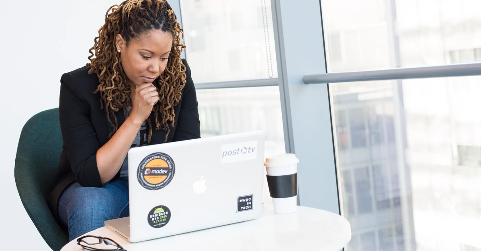 A business owner pausing in thought at a laptop, coffee in hand, waiting on results.