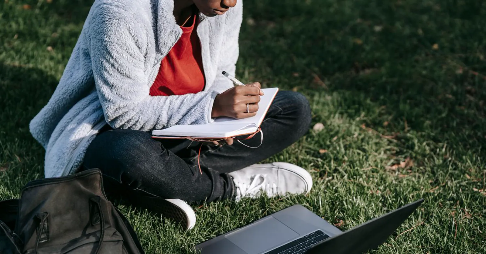 A young entrepreneur jotting research notes in a notebook beside a laptop.