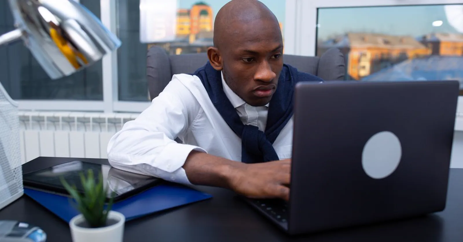 A focused entrepreneur working intently at a laptop by an office window.