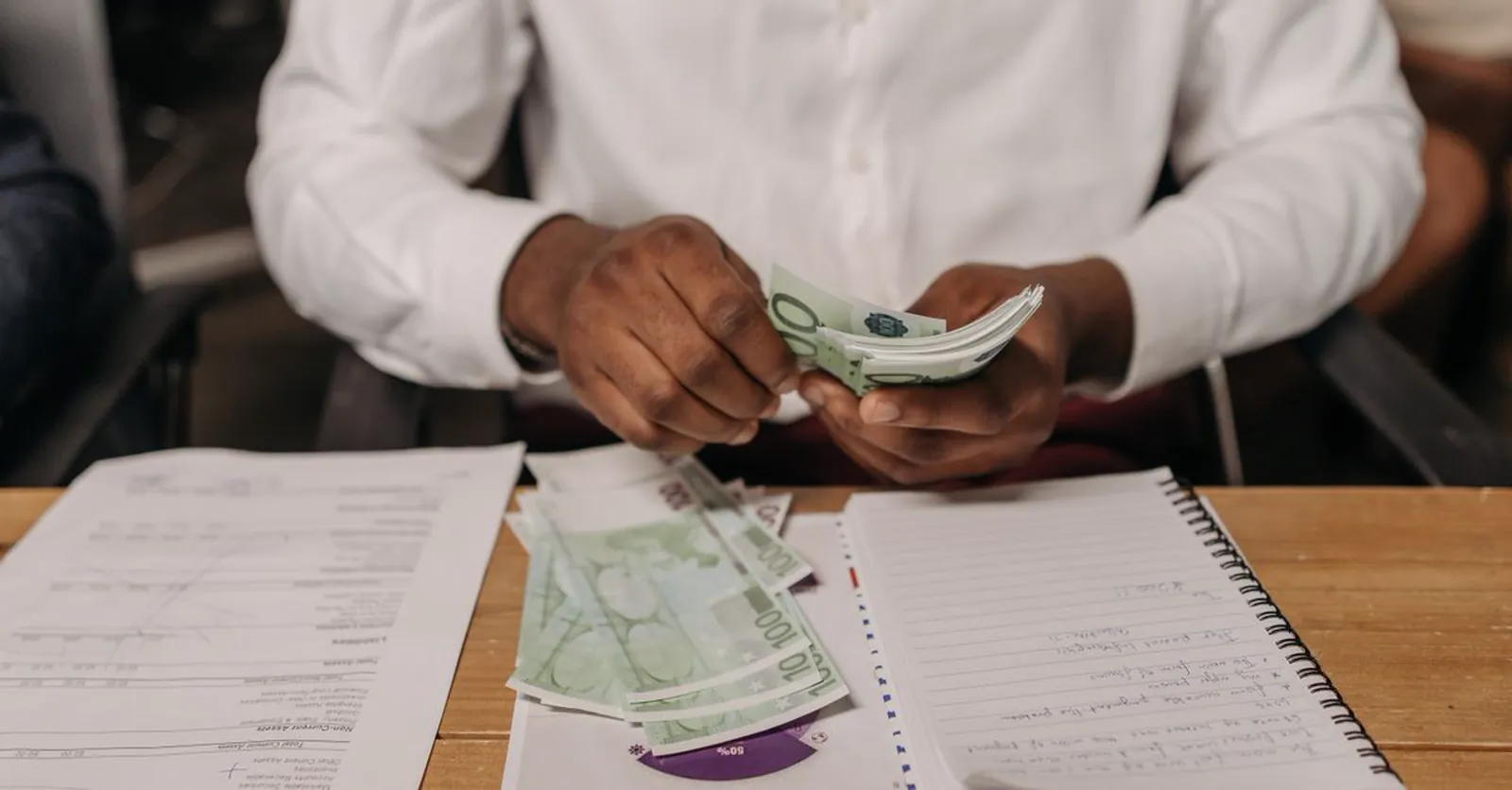 A business owner counting cash over financial statements and a notebook.