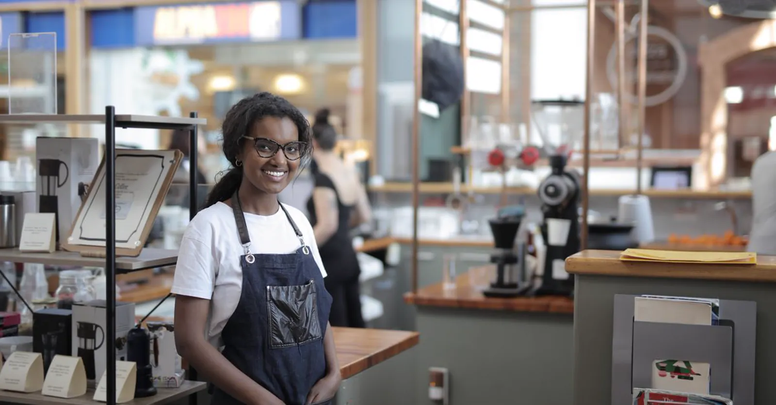A smiling café owner in an apron standing in her shop.