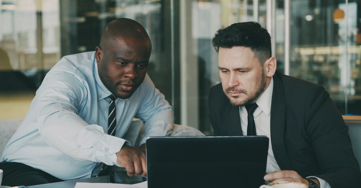 Two African business professionals comparing options on a laptop across a table in a meeting.