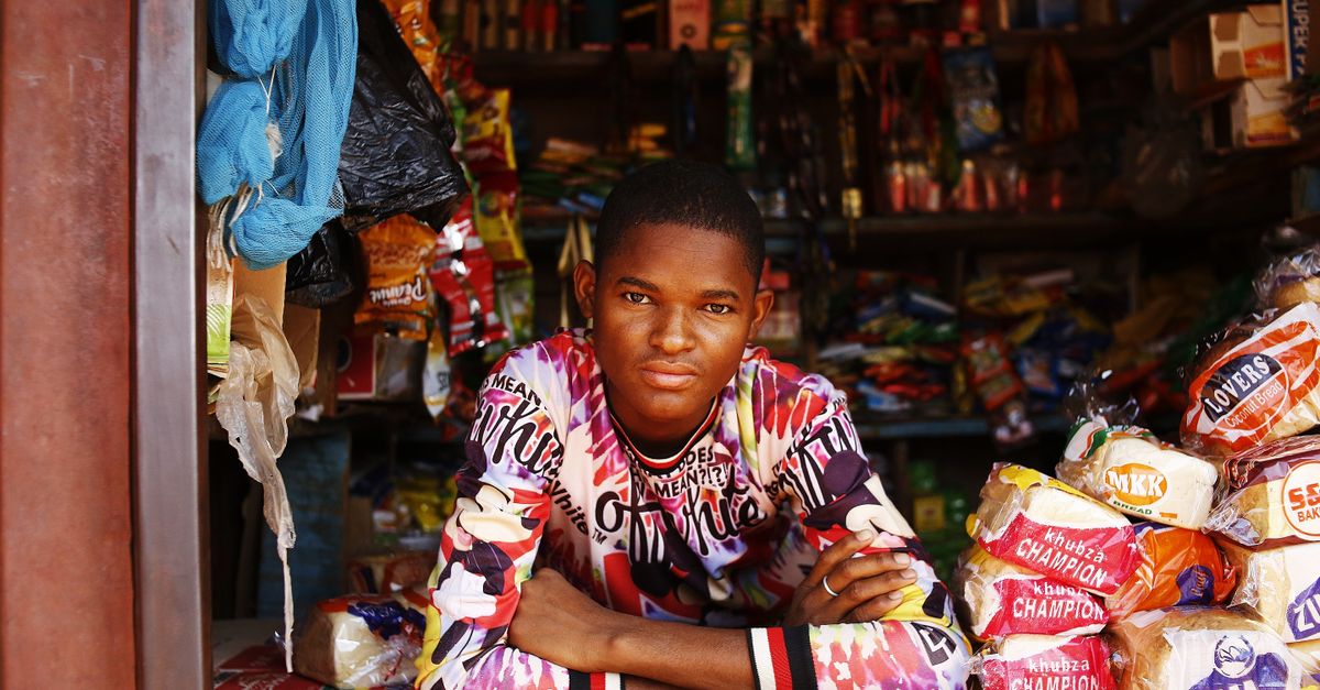A young African shop owner at his kiosk stocked with goods.